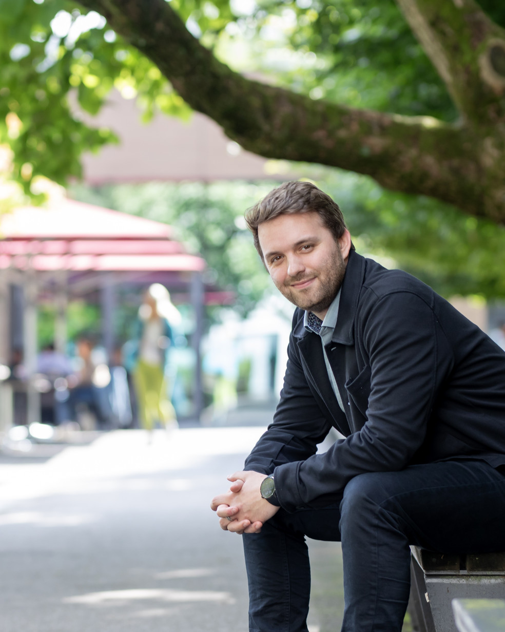 ein Mann in einer dunklen Jacke sitzt auf einer Bank in einem Park