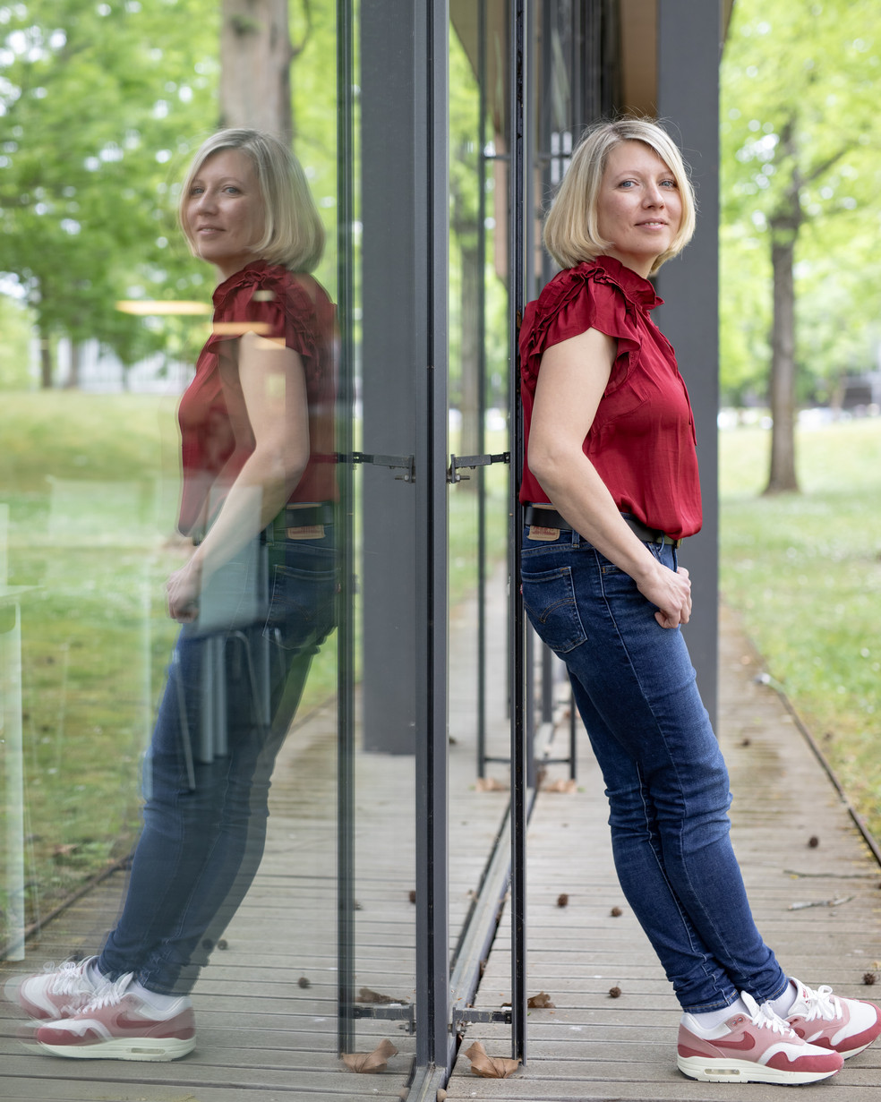 Junge blonde Frau in roter Bluse lehnt an einer Glasscheibe