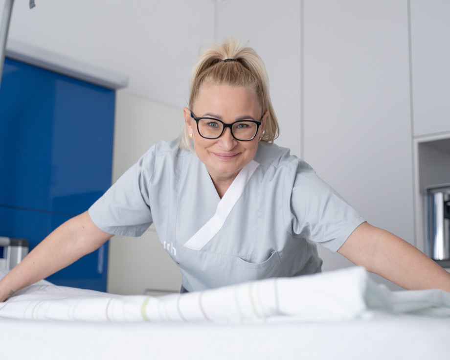 Eine Frau im Kasak beugt sich über ein Bett und lächelt