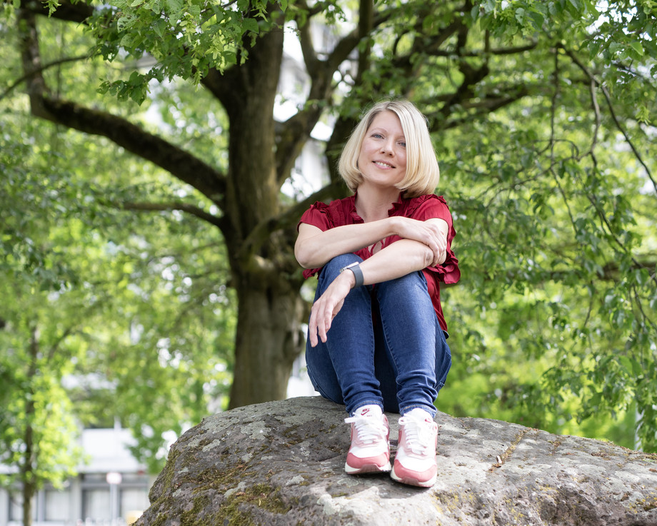 Junge Frau mit blonden Haaren sitzt auf einem Felsen