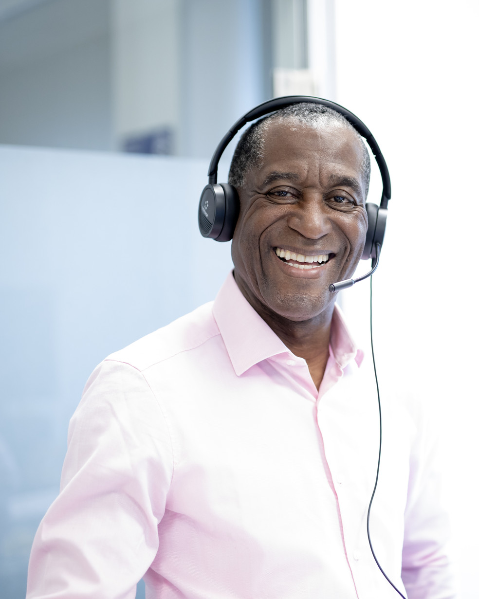 ein Mann in einem rosafarbenen Hemd sitzt mit einem Head Set im Büro