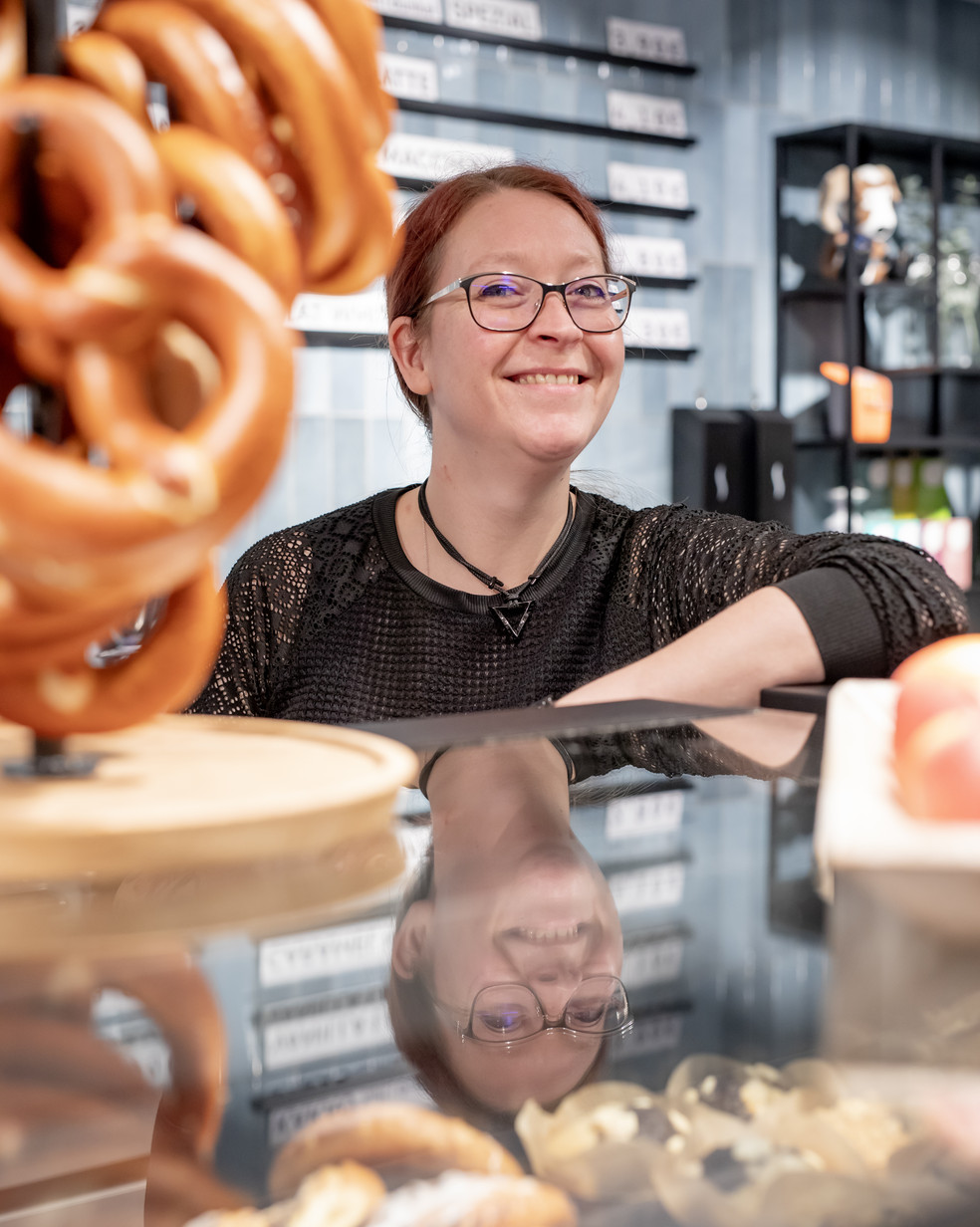 eine rotblonde Frau steht an einer Theke neben einem Brezelständer