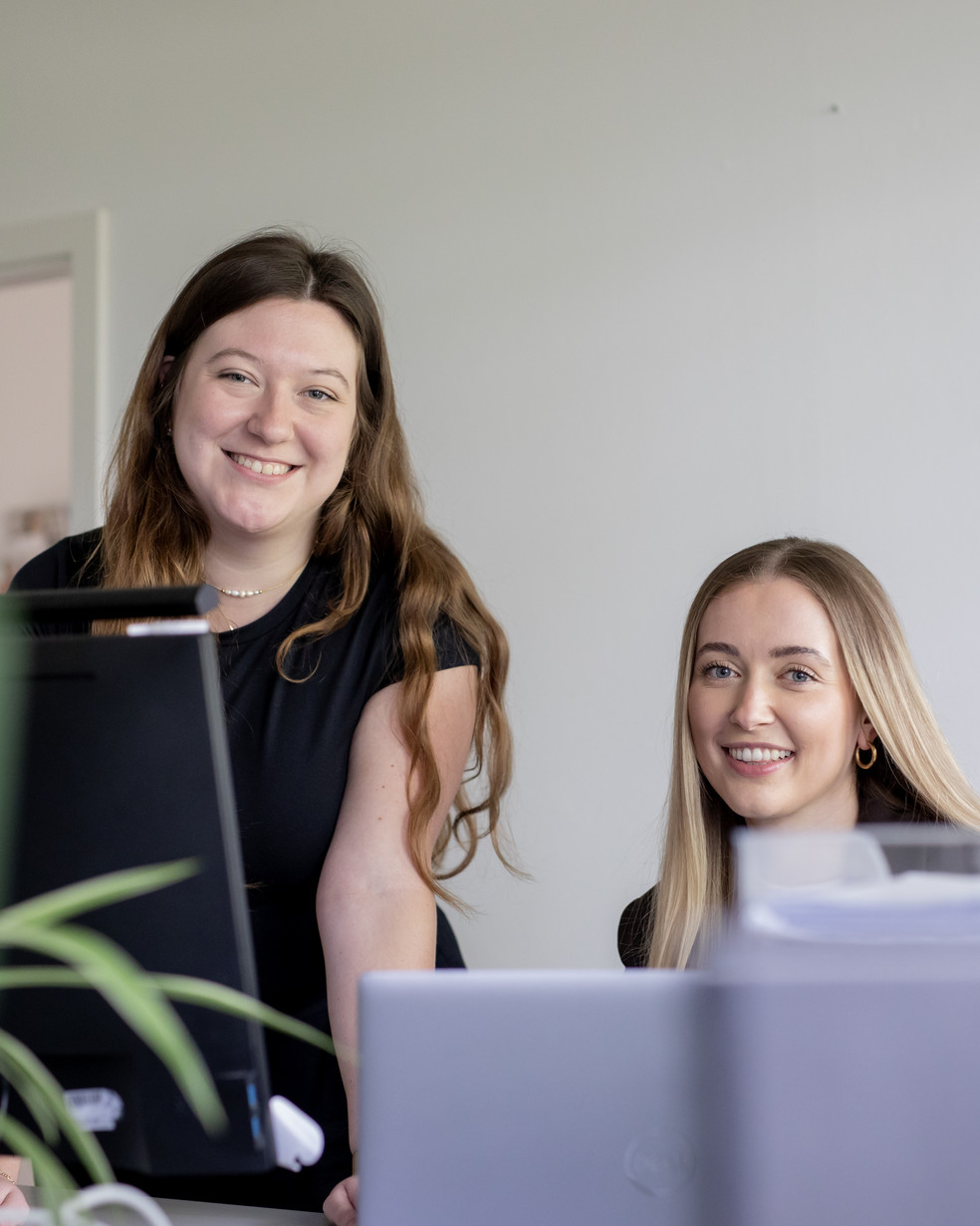 Zwei Frauen in einem Büro lächeln in die Kamera
