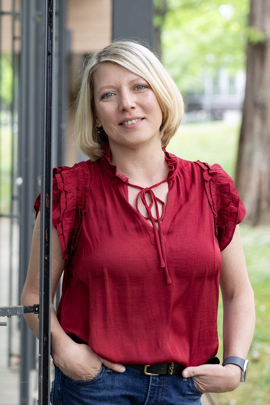 Blonde Frau in roter Bluse lehnt seitlich an einer Glasscheibe