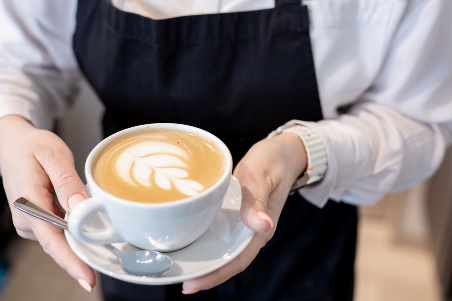 Person hält eine Tasse mit Milchkaffee und einem Milchschaummuster.